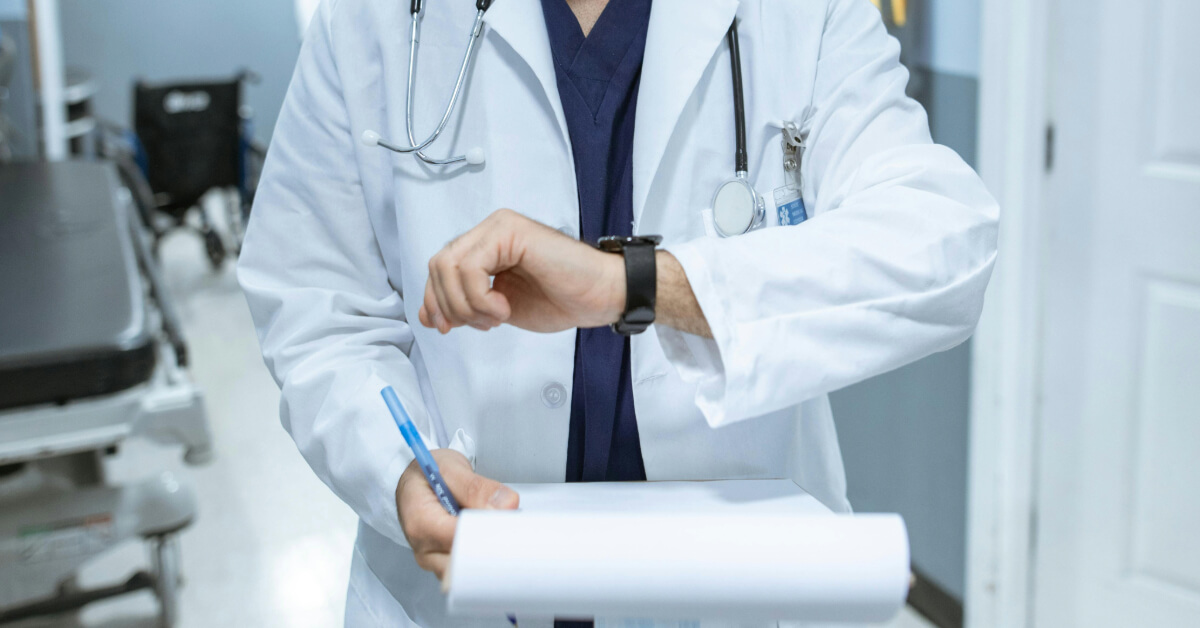 Doctor in lab coat checking wristwatch while holding medical chart.
