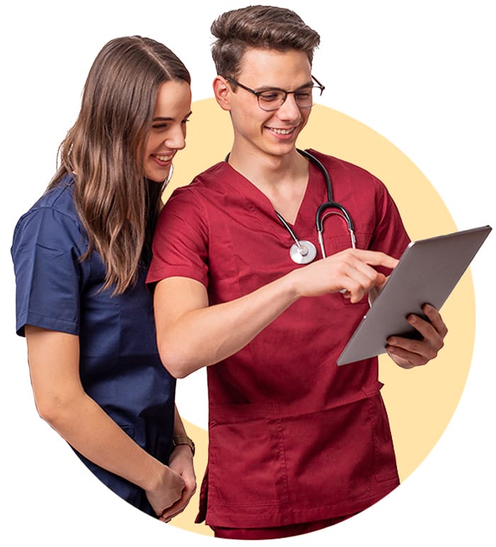 Two medical students in scrubs review a tablet.