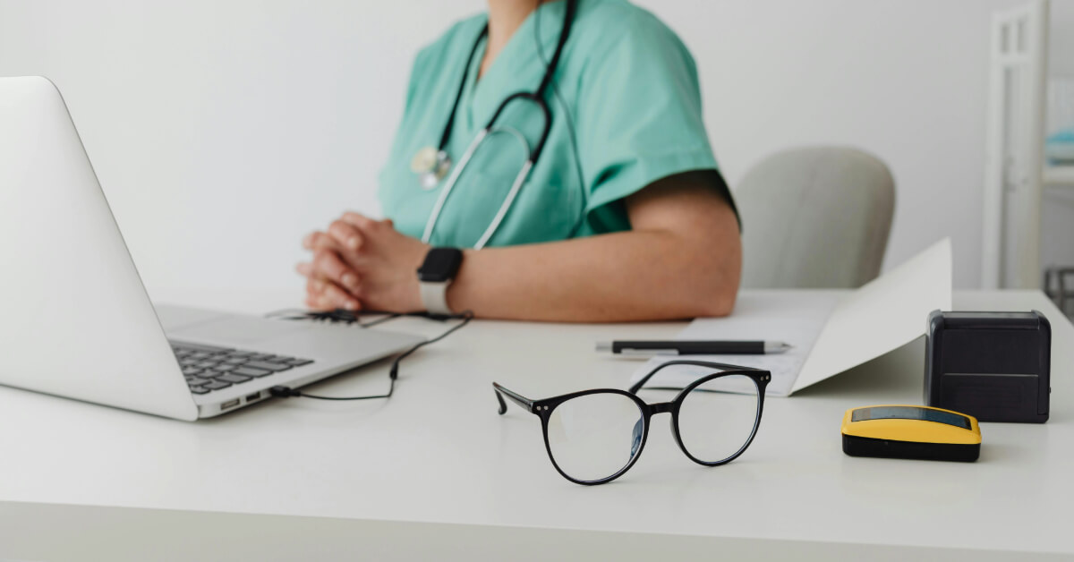 Nurse sitting behind a desk with a laptop and glasses.