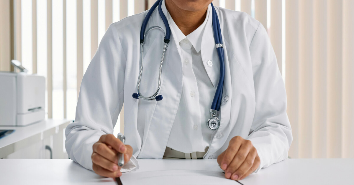 Doctor wearing a lab coat and a stethoscope sitting behind a desk
