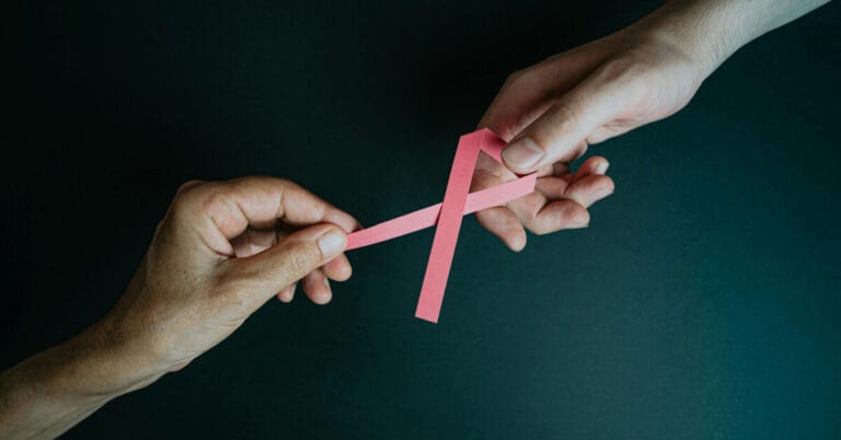 Two hands holding a cancer ribbon