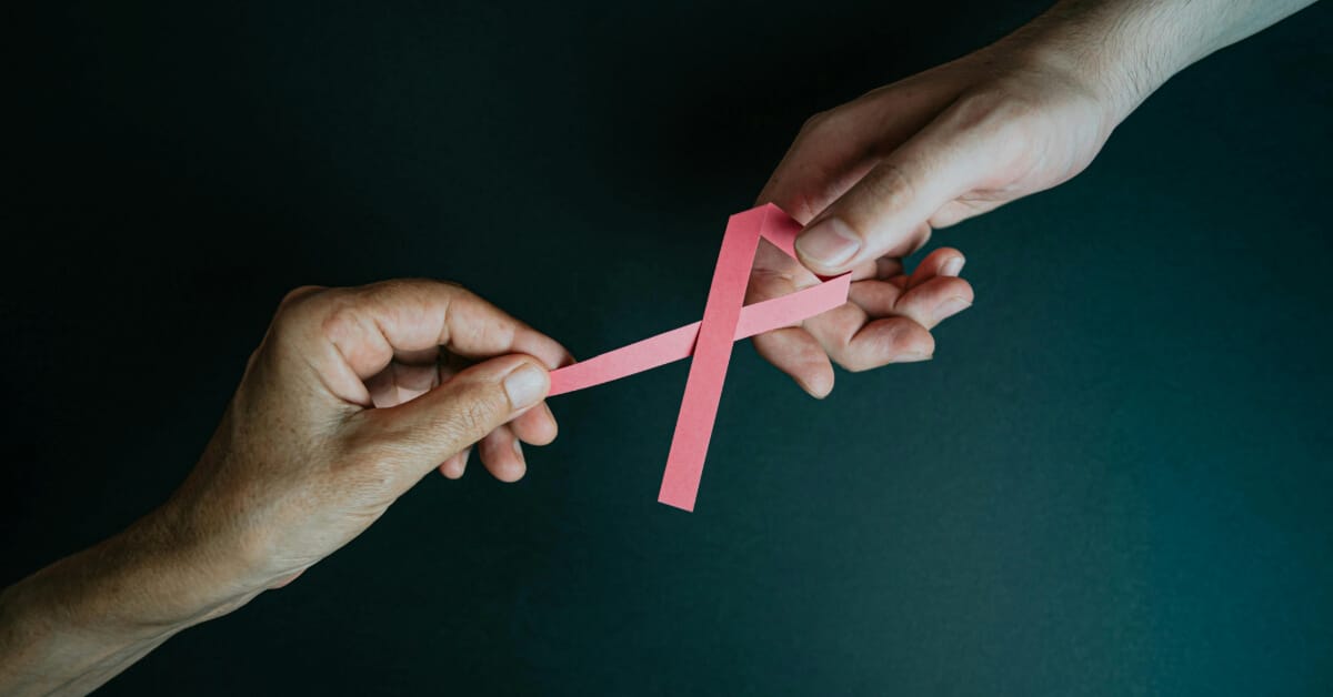 Two hands holding a cancer ribbon