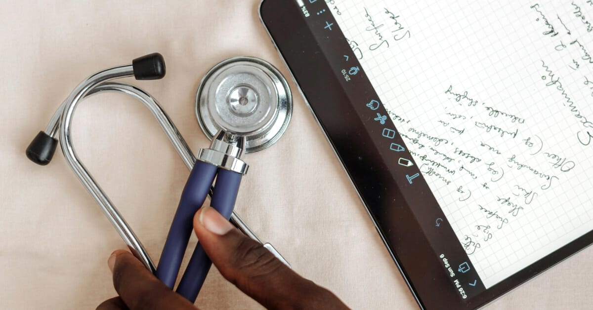 Person taking notes on a tablet with a stethoscope on the desk
